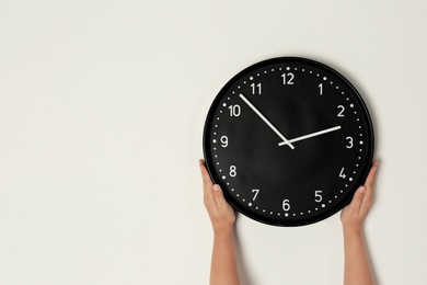 Woman touching clock on light wall, space for text. Time management