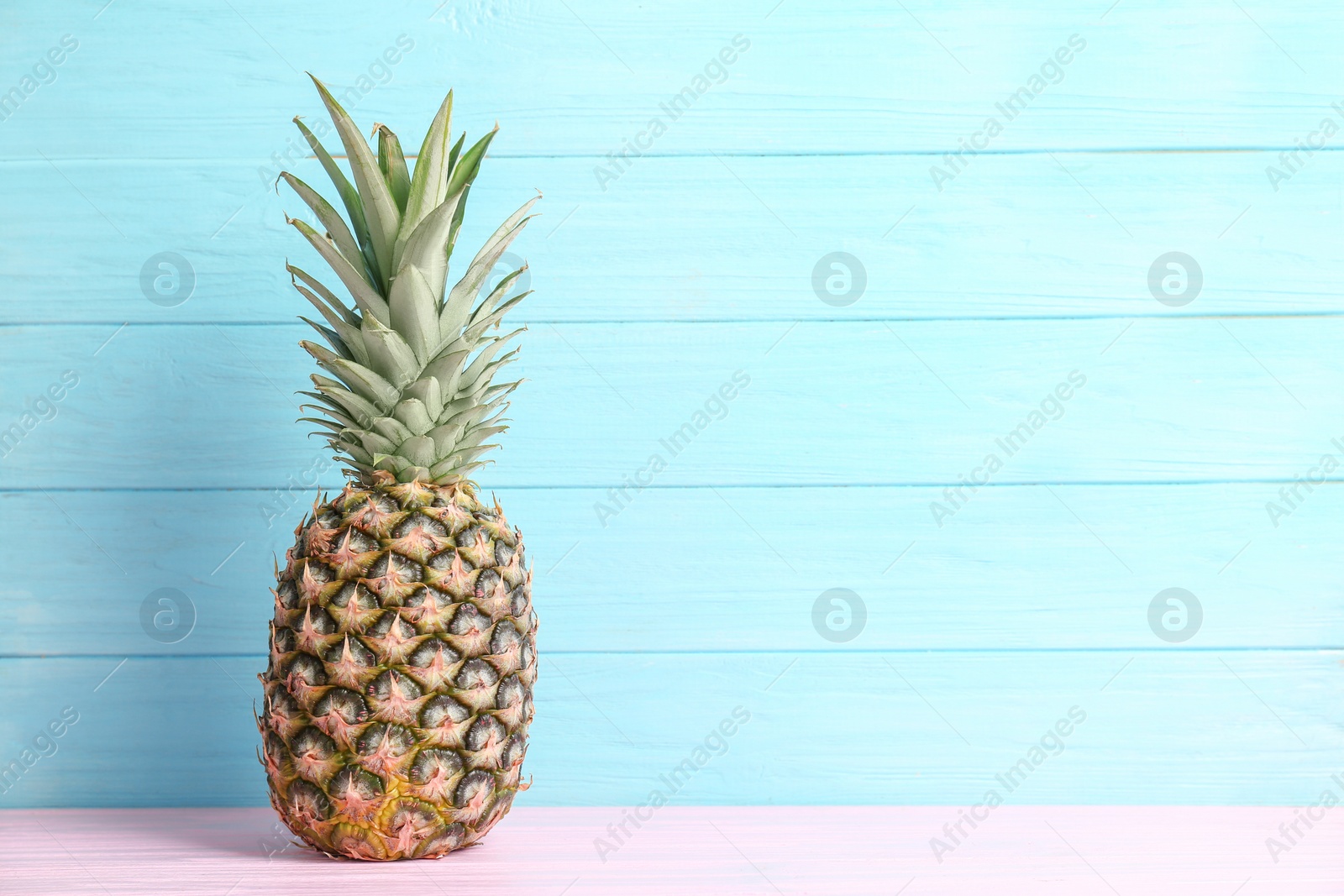 Photo of Fresh pineapple on table against color wall