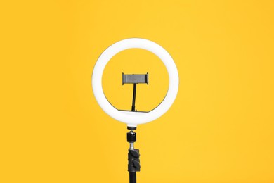 Photo of Modern tripod with ring light on yellow background