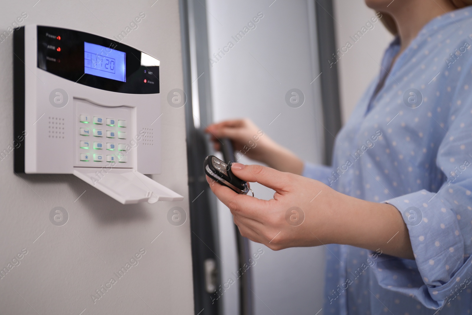 Photo of Woman with remote control near security alarm system on white wall, closeup