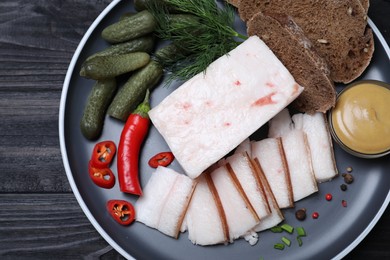 Photo of pork fatback with spices, rye bread and pickled cucumbers on black wooden table, top view