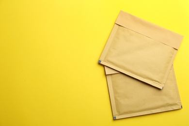 Photo of Kraft paper envelopes on yellow background, flat lay. Space for text