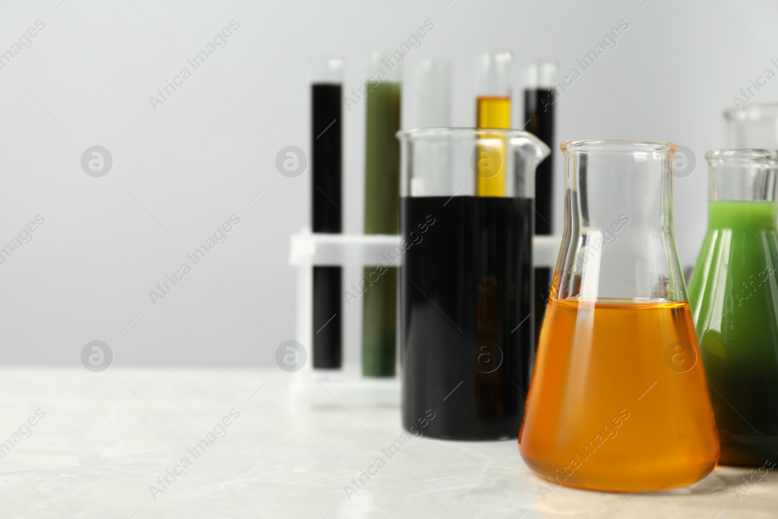 Photo of Laboratory glassware with different types of oil on white table, closeup. Space for text