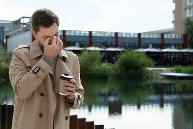 Photo of Sleepy man with cup of coffee near river outdoors. Space for text