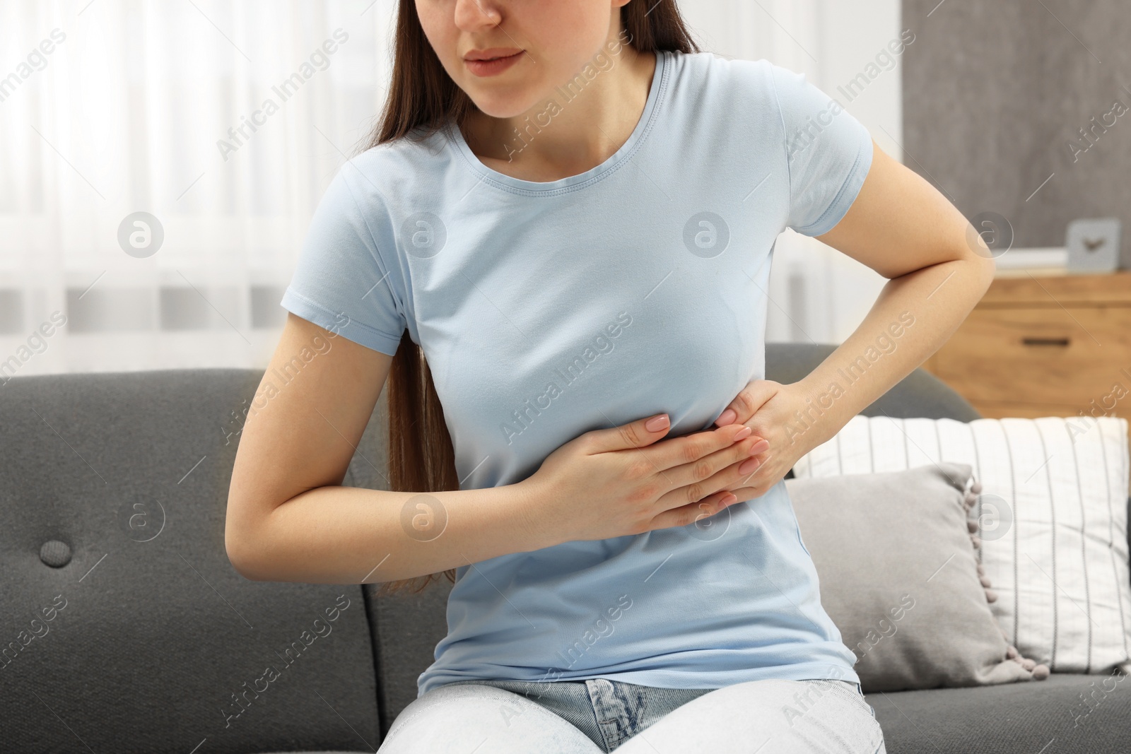 Photo of Woman suffering from stomach pain on sofa indoors, closeup