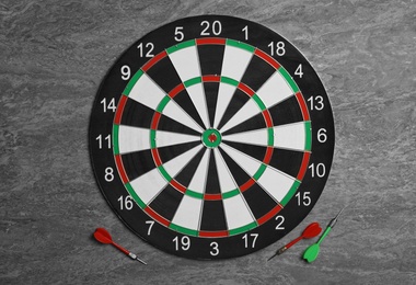 Dart board with color arrows on grey stone background, top view