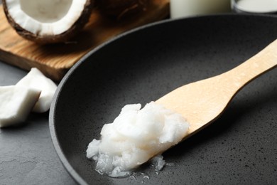 Photo of Frying pan with coconut oil and wooden spatula on table, closeup. Healthy cooking