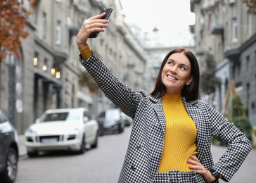 Photo of Beautiful woman in stylish suit taking selfie on city street