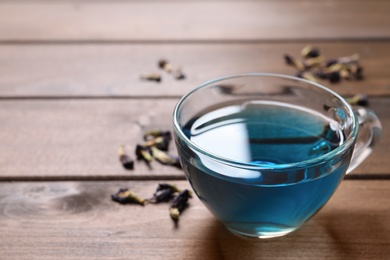 Photo of Glass cup of organic blue Anchan on wooden table, space for text. Herbal tea