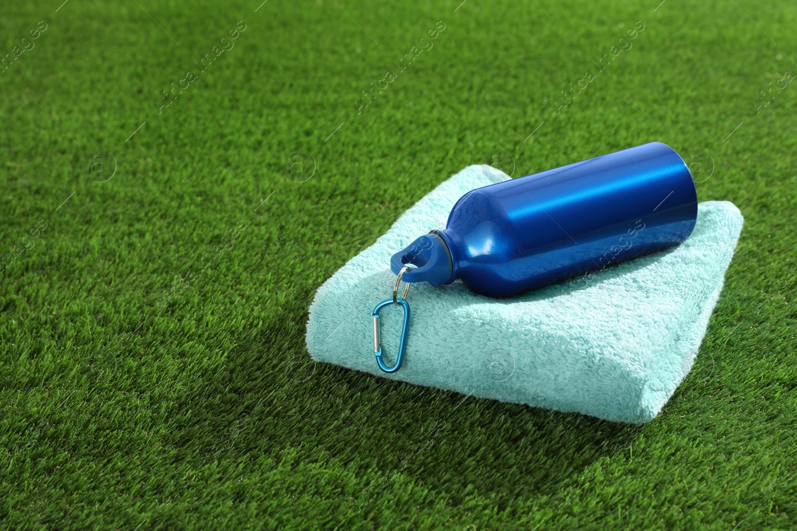 Photo of Bottle of water, towel and space for text on artificial grass. Fitness equipment