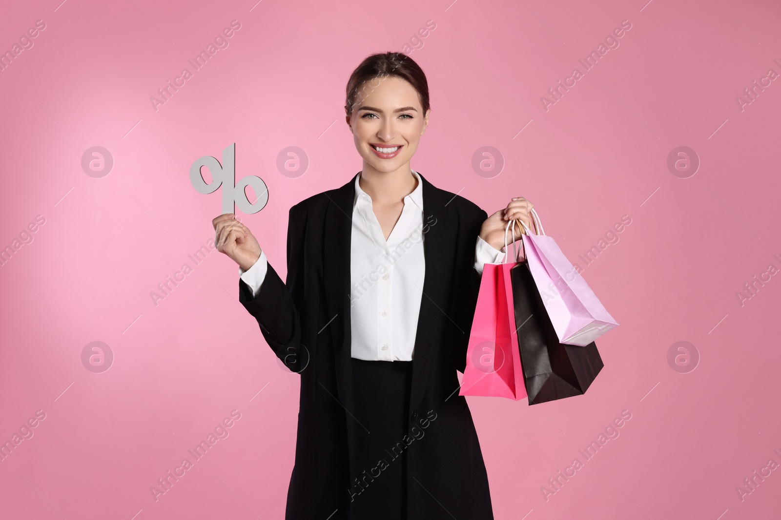 Photo of Happy young woman with shopping bags and percent symbol figure on light pink background. Big sale