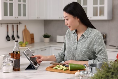 Photo of Beautiful woman searching recipe on tablet while cooking in kitchen