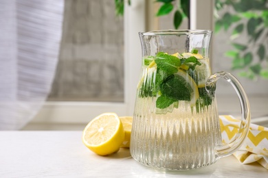 Tasty refreshing lemonade in jug on white table indoors