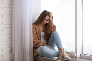 Photo of Upset teenage girl sitting alone near window indoors