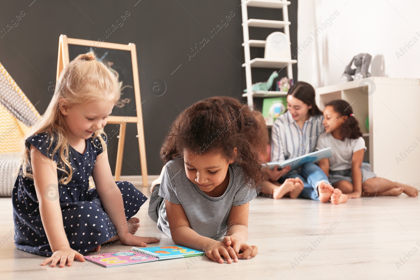 Photo of Cute little children reading book on floor in kindergarten, space for text. Indoor activity
