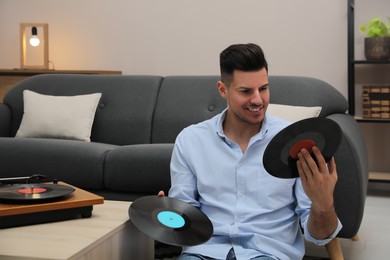 Happy man choosing vinyl record to play with turntable at home