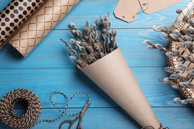 Beautiful bouquet of pussy willow branches and wrapping materials on light blue wooden table, flat lay