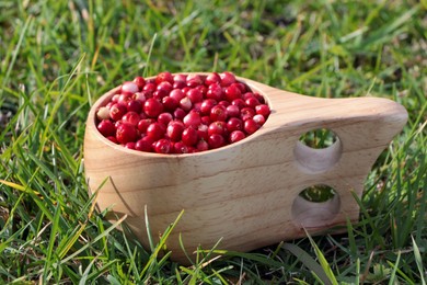 Photo of Wooden cup with tasty ripe lingonberries on green grass outdoors, closeup