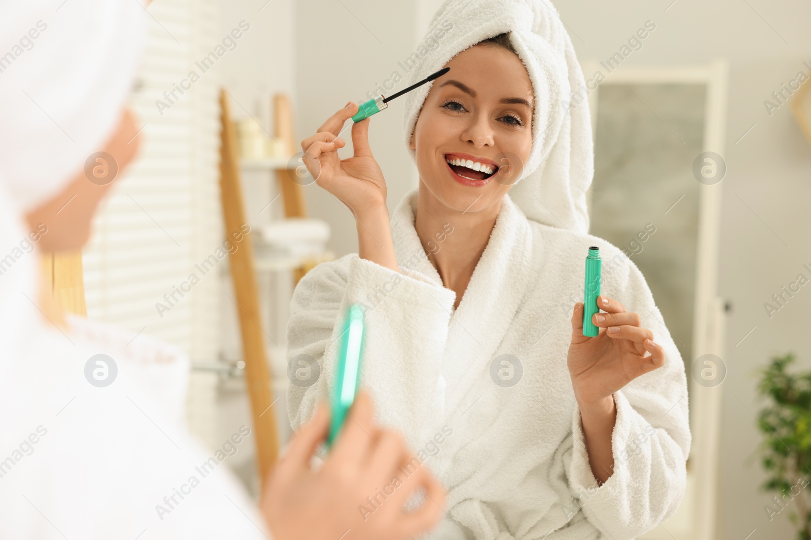 Photo of Beautiful woman applying mascara near mirror in bathroom