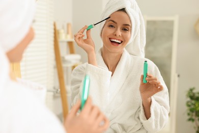 Beautiful woman applying mascara near mirror in bathroom