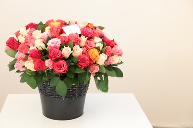 Photo of Bouquet of beautiful roses with blank card on white table against light background, space for text