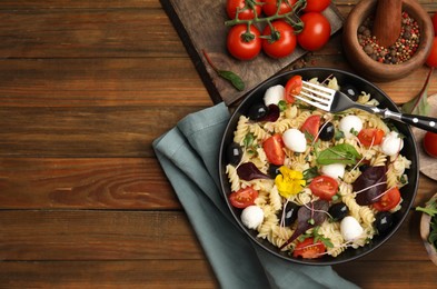 Bowl of delicious pasta with tomatoes, olives and mozzarella on wooden table, flat lay. Space for text