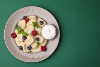 Plate of tasty lazy dumplings with berries, mint leaves and sour cream on dark green background, top view. Space for text