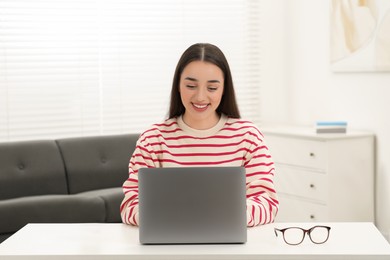 Photo of Woman using laptop at white table indoors