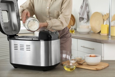 Making dough. Woman adding flour into breadmaker machine at wooden table, closeup