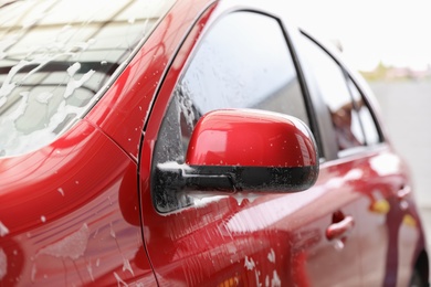 Photo of Red auto with foam at car wash. Cleaning service