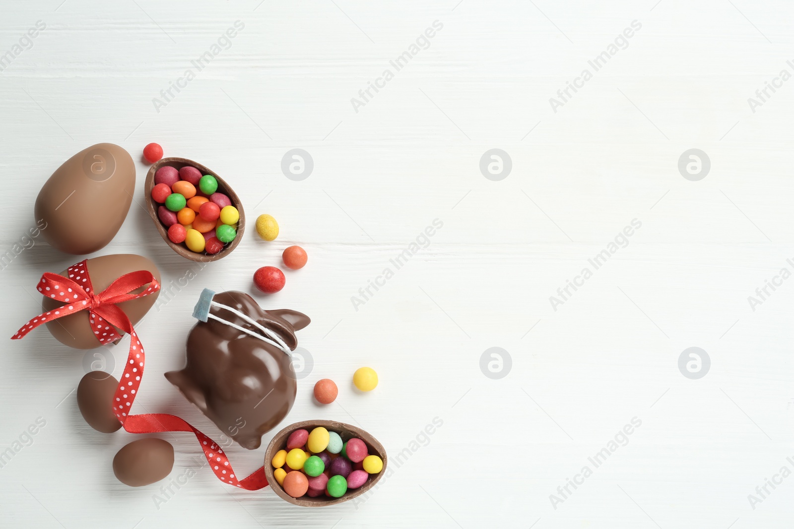 Photo of Chocolate bunny with protective mask, eggs and space for text on white wooden table, flat lay. Easter holiday during COVID-19 quarantine