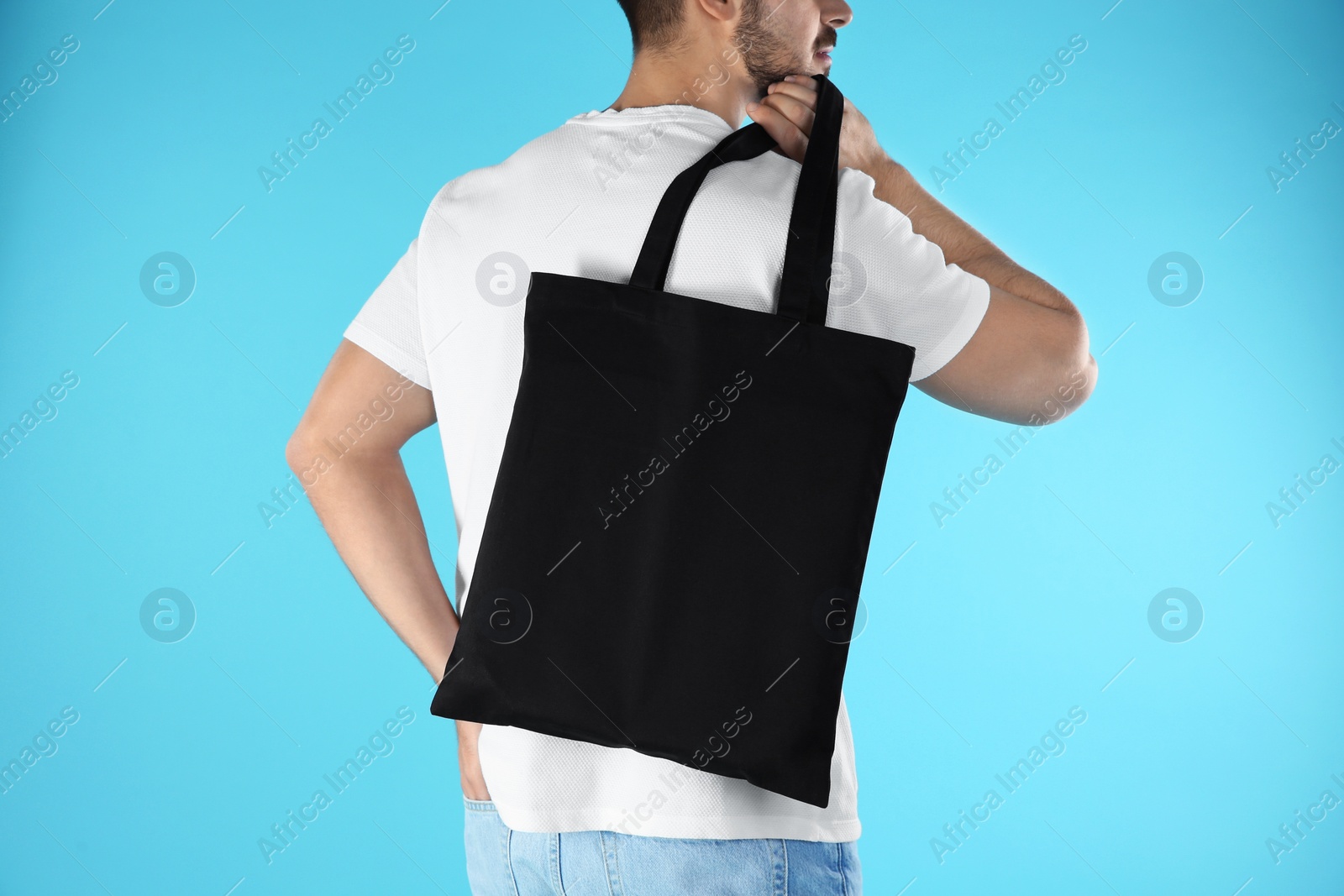 Photo of Young man holding textile bag on color background, closeup. Mockup for design