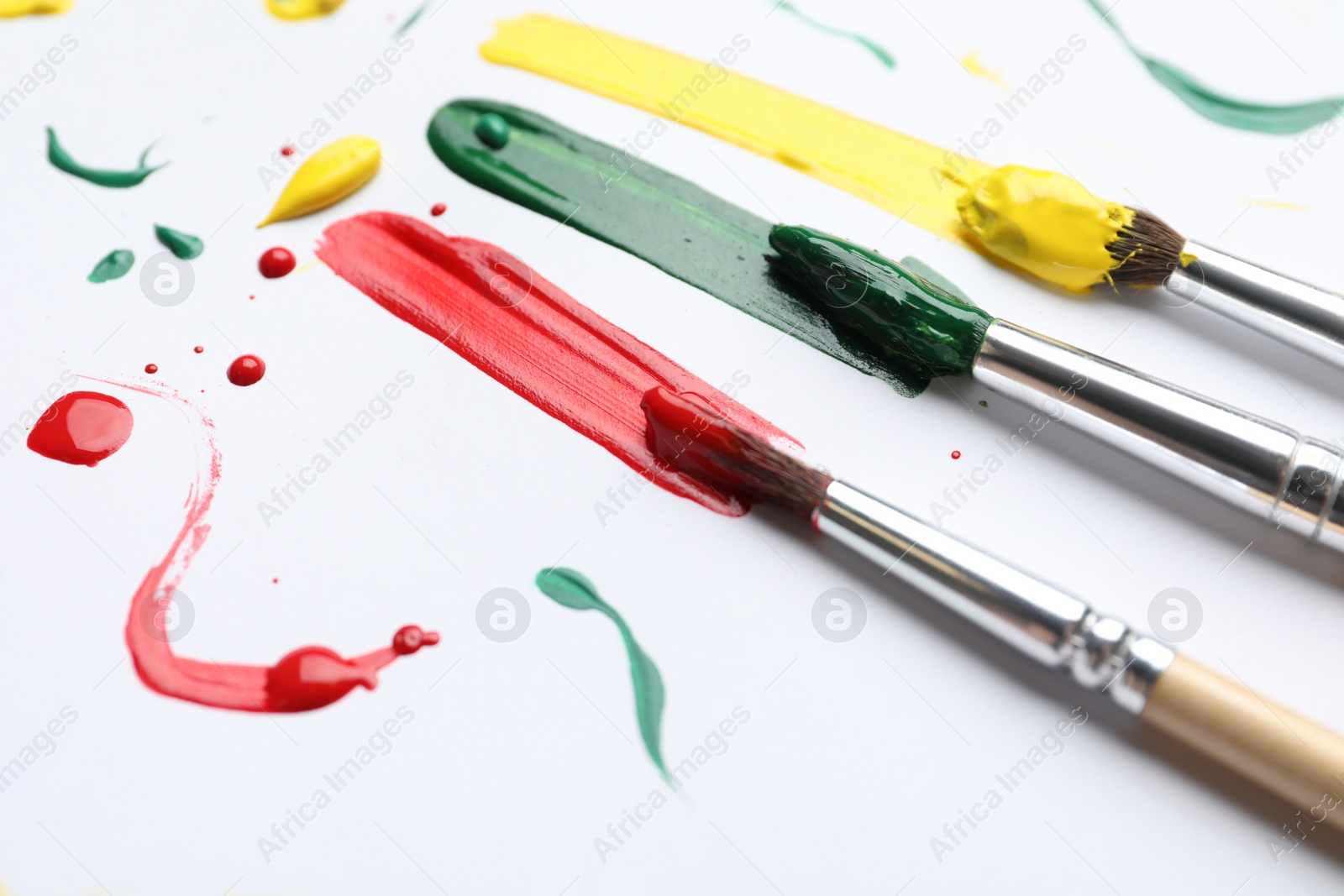 Photo of Brushes with different paints and strokes on white background, closeup