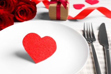 Photo of Beautiful dishware with heart, gift and bouquet on white wooden table, closeup. Romantic date