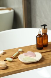 Jade and rose quartz gua sha tools, natural face roller with cosmetic products on wooden caddy in bathroom