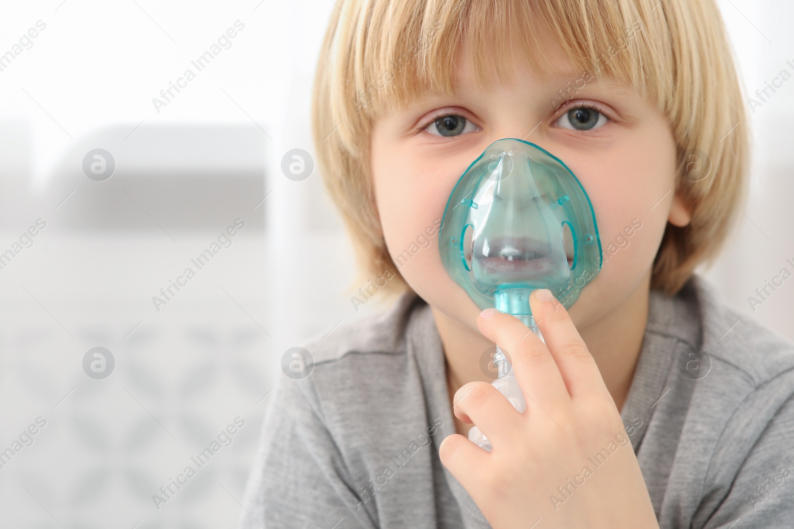 Photo of Sick little boy using nebulizer for inhalation indoors