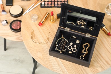 Photo of Jewelry box with stylish golden bijouterie and makeup products on wooden table, above view