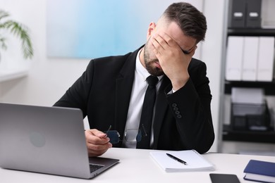 Overwhelmed man at table with laptop in office