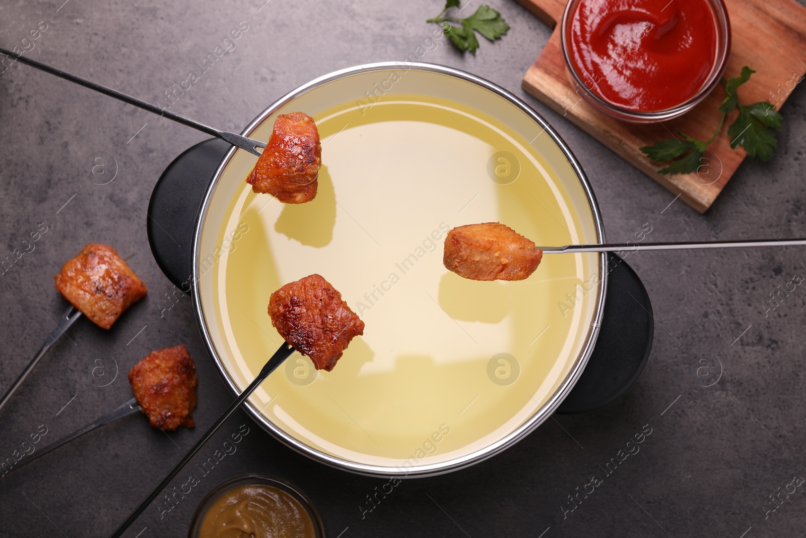 Photo of Oil in fondue pot, forks with fried meat pieces and sauces on grey table, flat lay