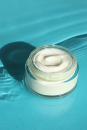 Jar with moisturizing cream in water on light blue background