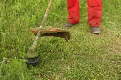 Worker cutting grass with string trimmer outdoors, closeup view