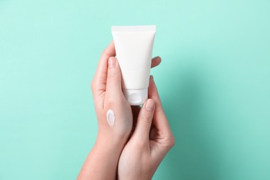 Photo of Woman with tube of hand cream on turquoise background, closeup