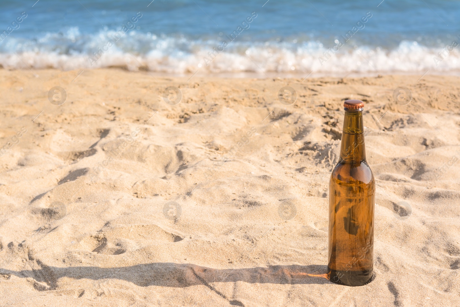 Photo of Bottle of beer on sandy beach near sea. Space for text