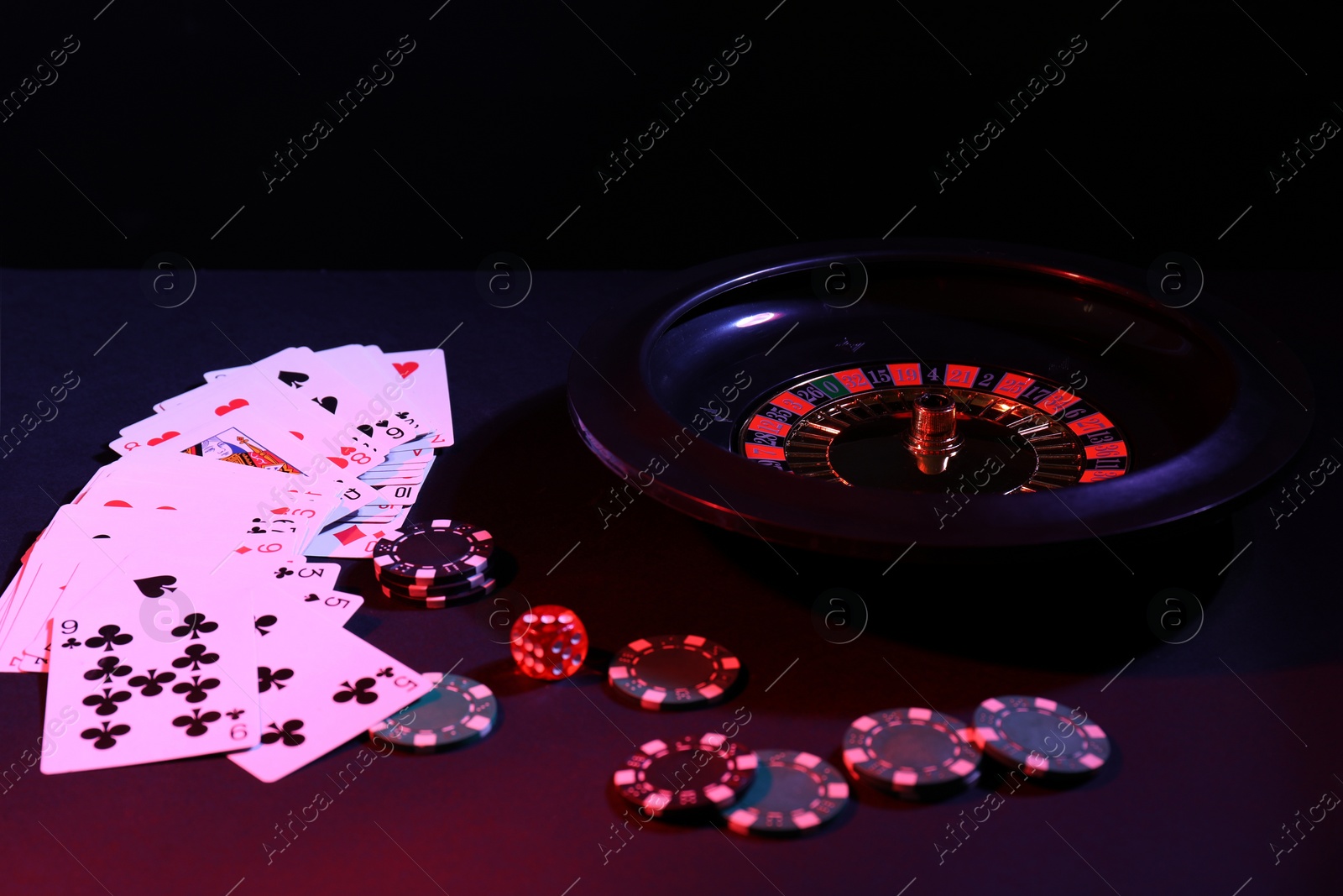 Photo of Roulette wheel with ball, chips, dice and playing cards on dark table, closeup. Casino game