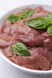 Photo of Bowl with raw chicken liver and basil on white table, closeup