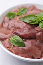 Bowl with raw chicken liver and basil on white table, closeup