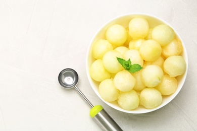 Photo of Bowl of melon balls with mint on light table, top view. Space for text