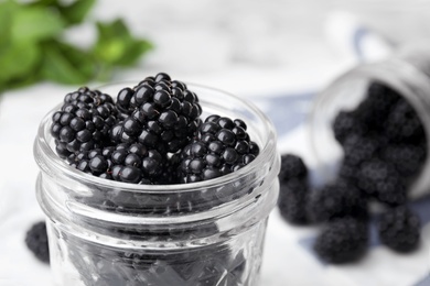 Photo of Glass jar of tasty ripe blackberries on table, closeup