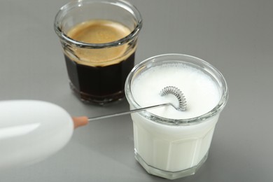 Whisking milk in glass with mini mixer (milk frother) on grey background, closeup