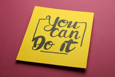 Photo of Yellow card with motivational phrase You Can Do It on burgundy background